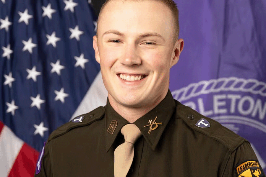 Tarleton cadet in uniform smiles for a portrait in front of the U.S. and Tarleton State University flags.